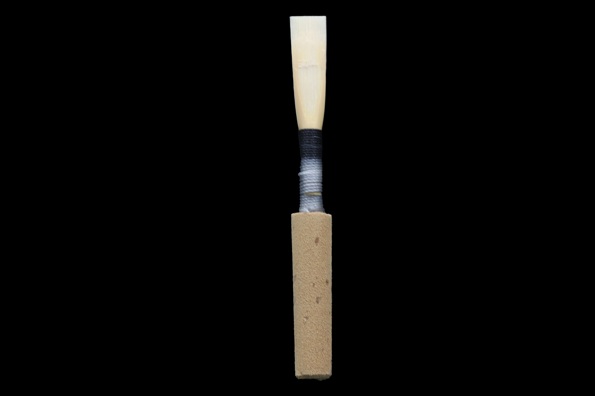 A single Treasure State oboe reed with a metal staple and thread ligature, isolated on a black background.